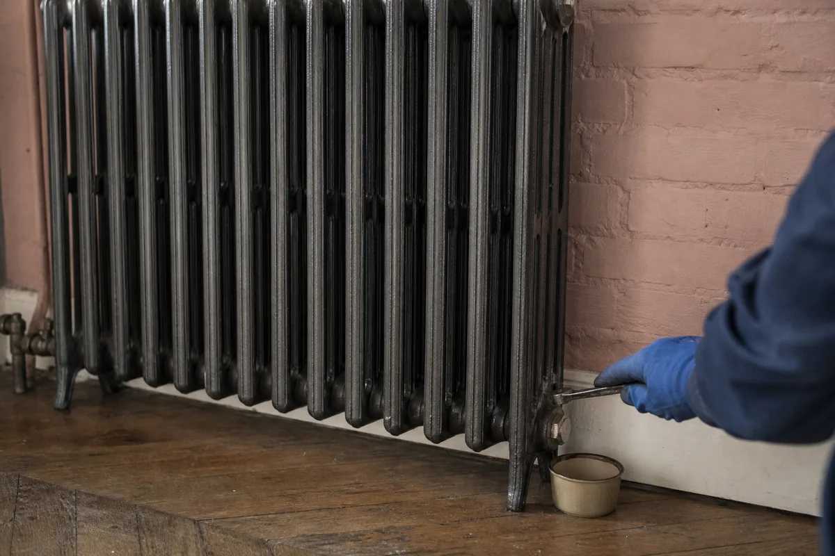 Radiateur en fonte purgé dans un salon de maison en brique rouge, lumière grise de matin d’hiver