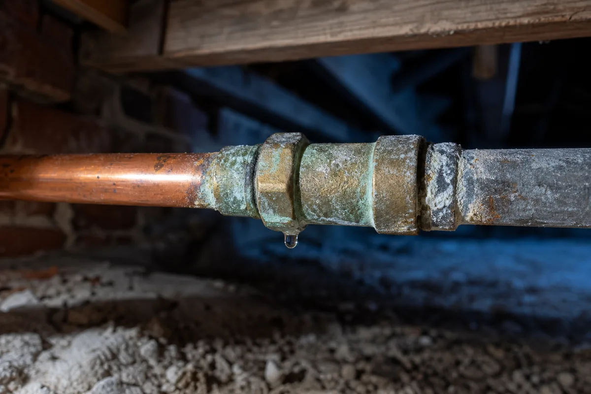 Raccord en cuivre corrodé sur une canalisation ancienne dans un vide sanitaire de maison en brique