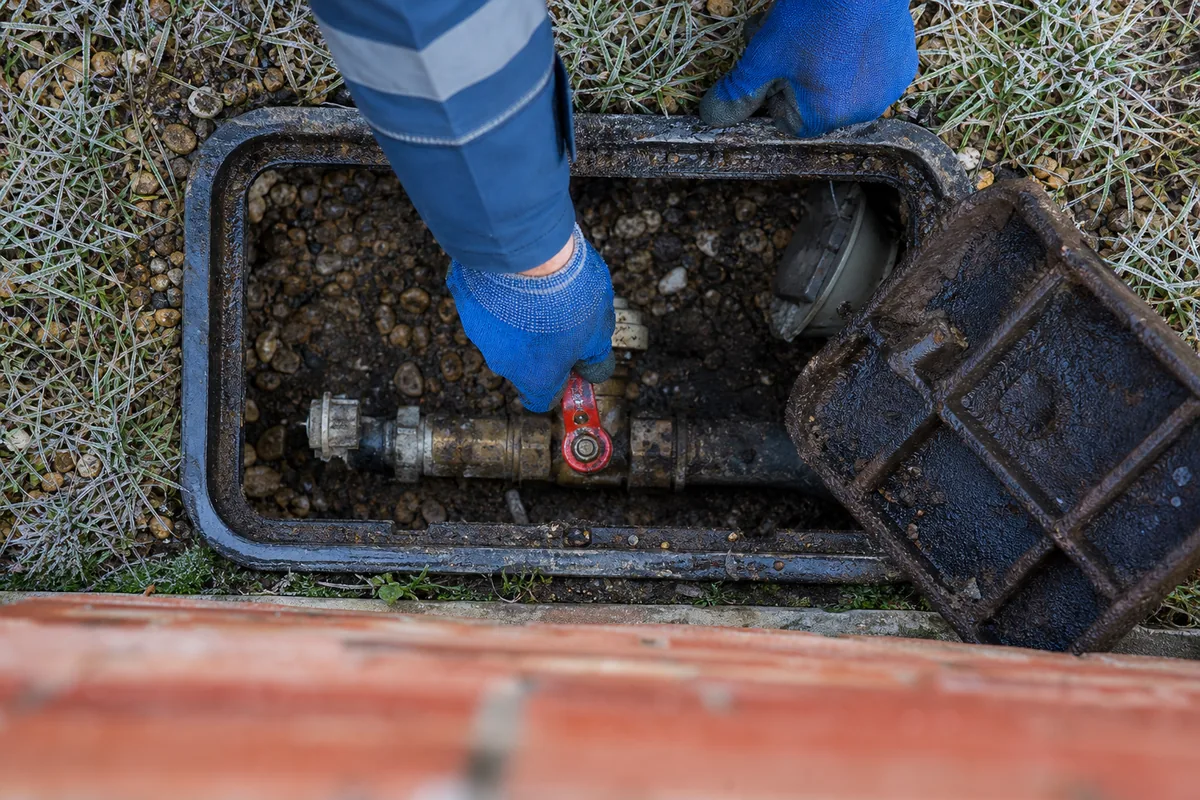 Mains gantées refermant une vanne quart de tour sur un compteur d&rsquo;eau en regard extérieur