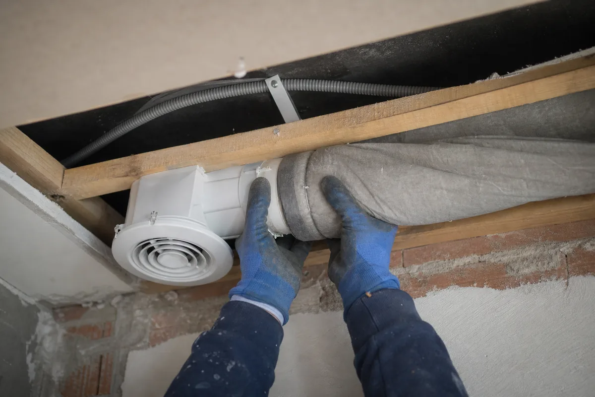 Extracteur d&rsquo;air et gaine souple posés au plafond d&rsquo;une salle d&rsquo;eau sans fenêtre