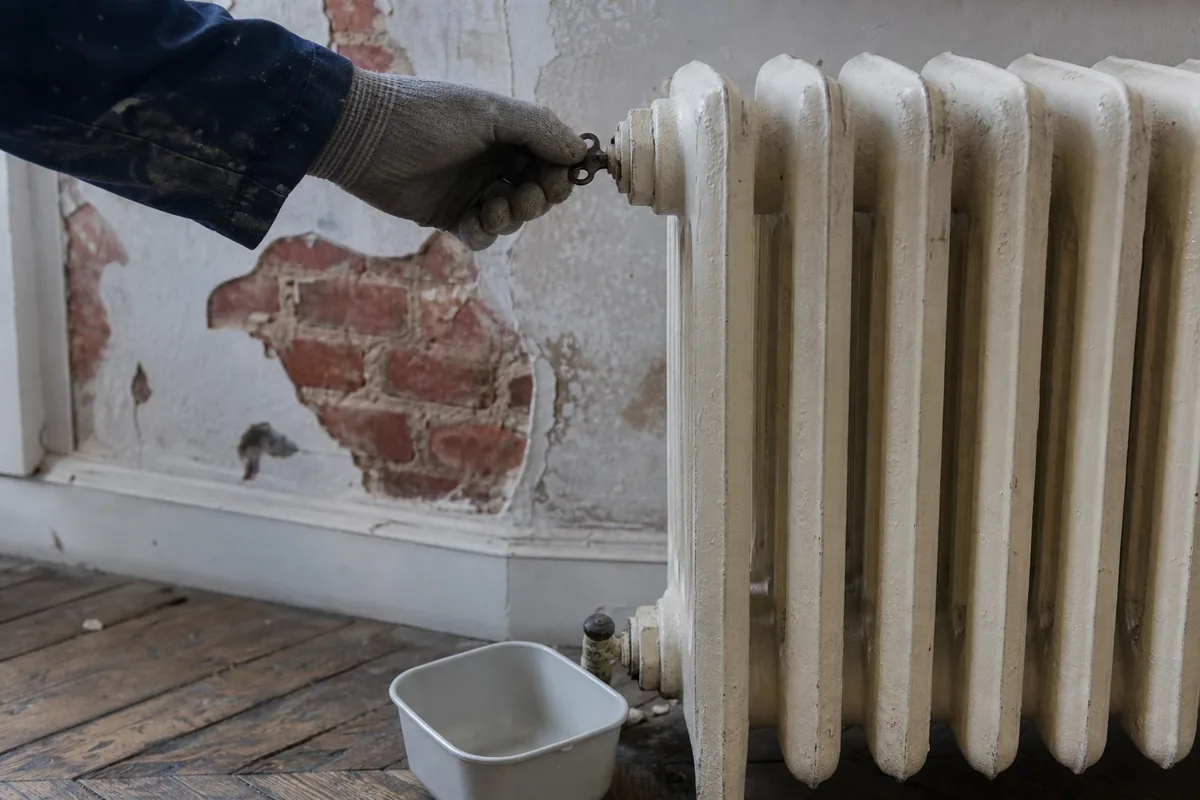 Radiateur en fonte purgé dans un salon de maison en brique rouge